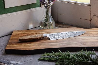 Decorative chef's knife on a wooden cutting board with a vase and flowers in the background.