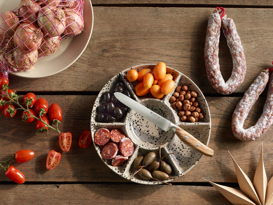 Assorted meats, olives, and vegetables on a wooden table with a ceramic dish.