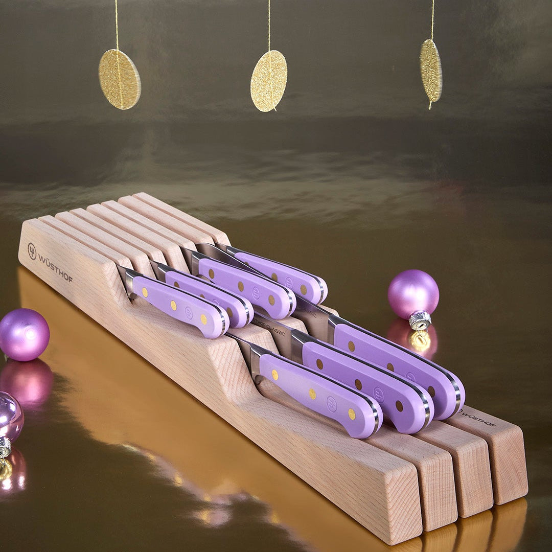 Set of purple knives with wooden handles on a wooden stand against a reflective surface background.