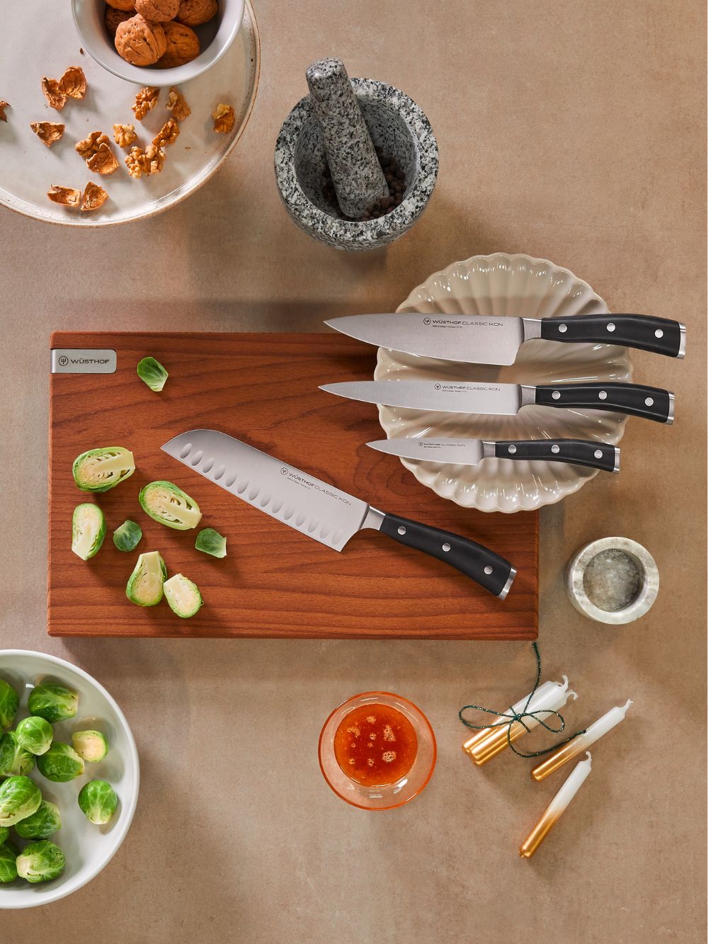 Set of knives on a wooden cutting board with vegetables and kitchen items on a brown surface