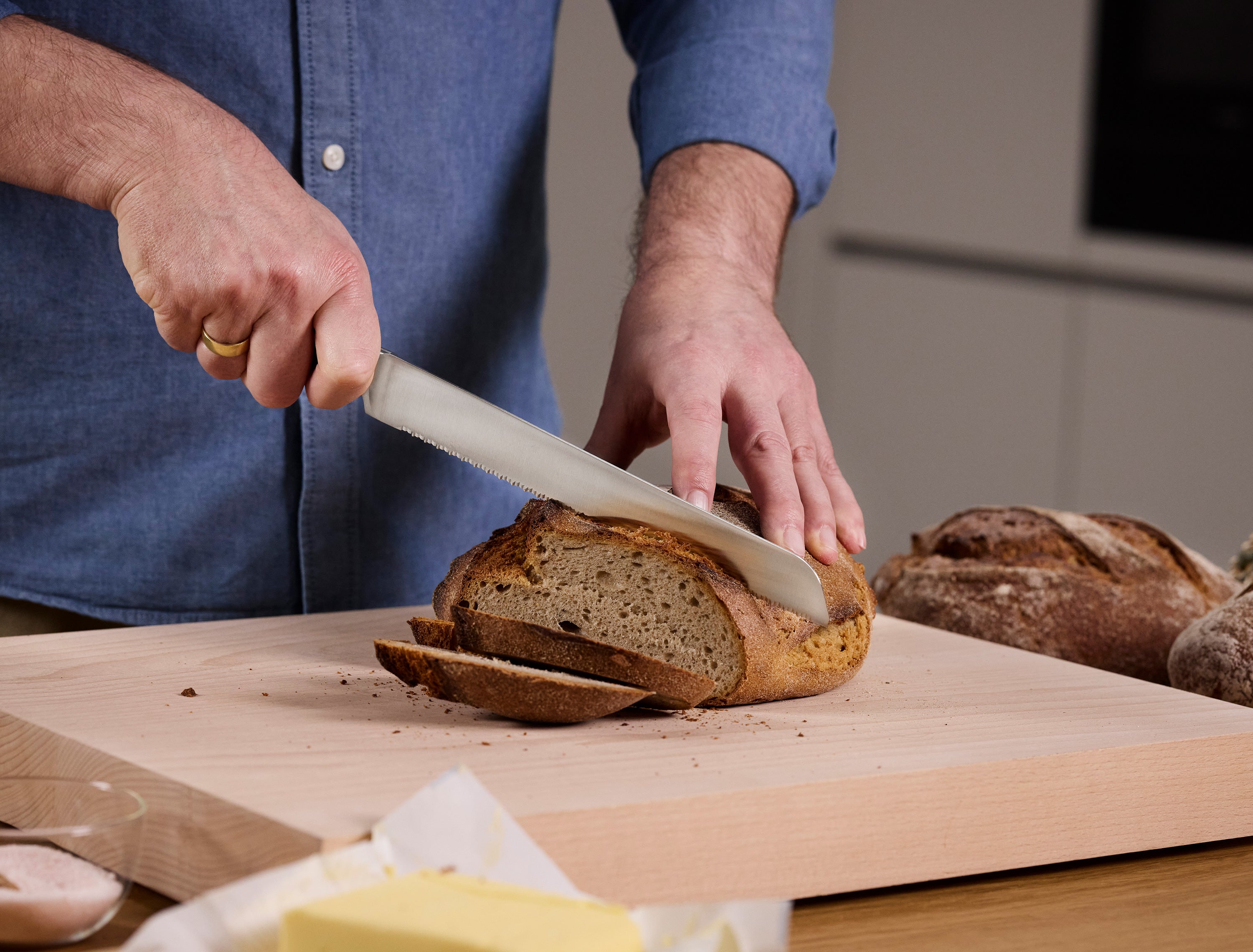 Person slicing bread on a wooden cutting board with a kitchen setting in the background.