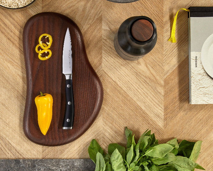 Wooden cutting board with knife, yellow peppers, and spinach on a wooden surface.
