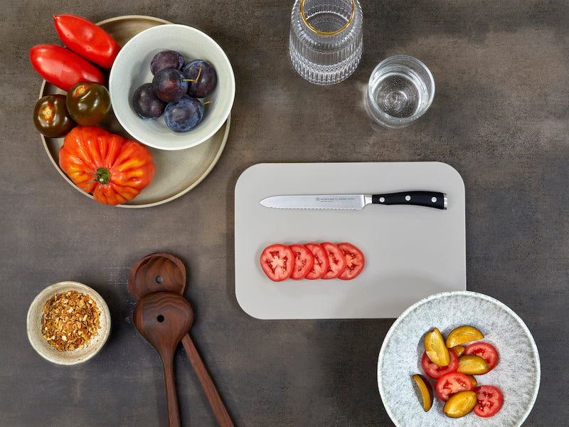 knife on cutting board surrounded by tomatoes on a concrete counter