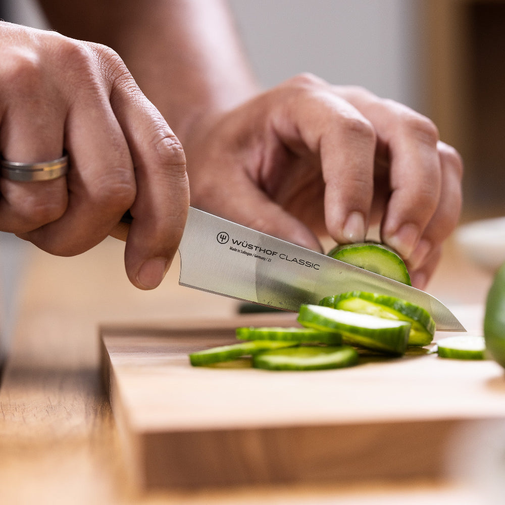 Person slicing cucumbers on a wooden cutting board with a knife.