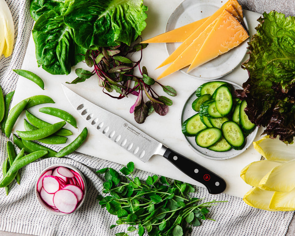 craftsman knife on cutting board with assorted vegetables and cheeses