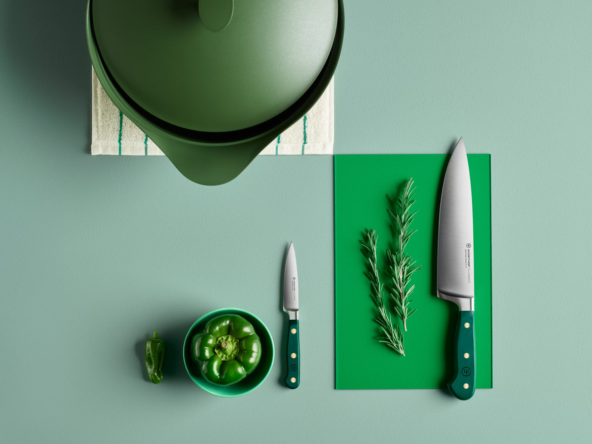 Green kitchen items including a pot, cutting board, knives, and herbs on a green surface