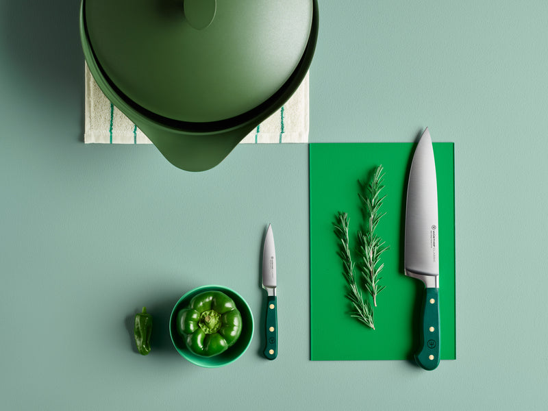 Green kitchen items including a pot, cutting board, knives, and herbs on a green surface