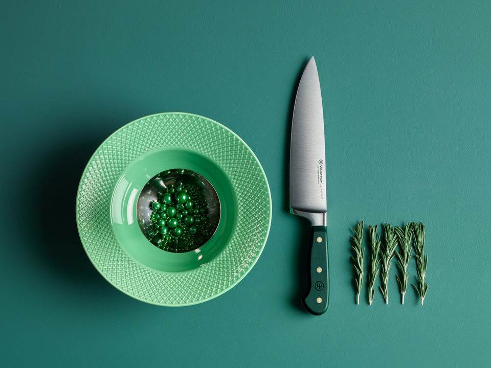 A green bowl with beads, a chef's knife, and sprigs of rosemary neatly arranged on a green surface.