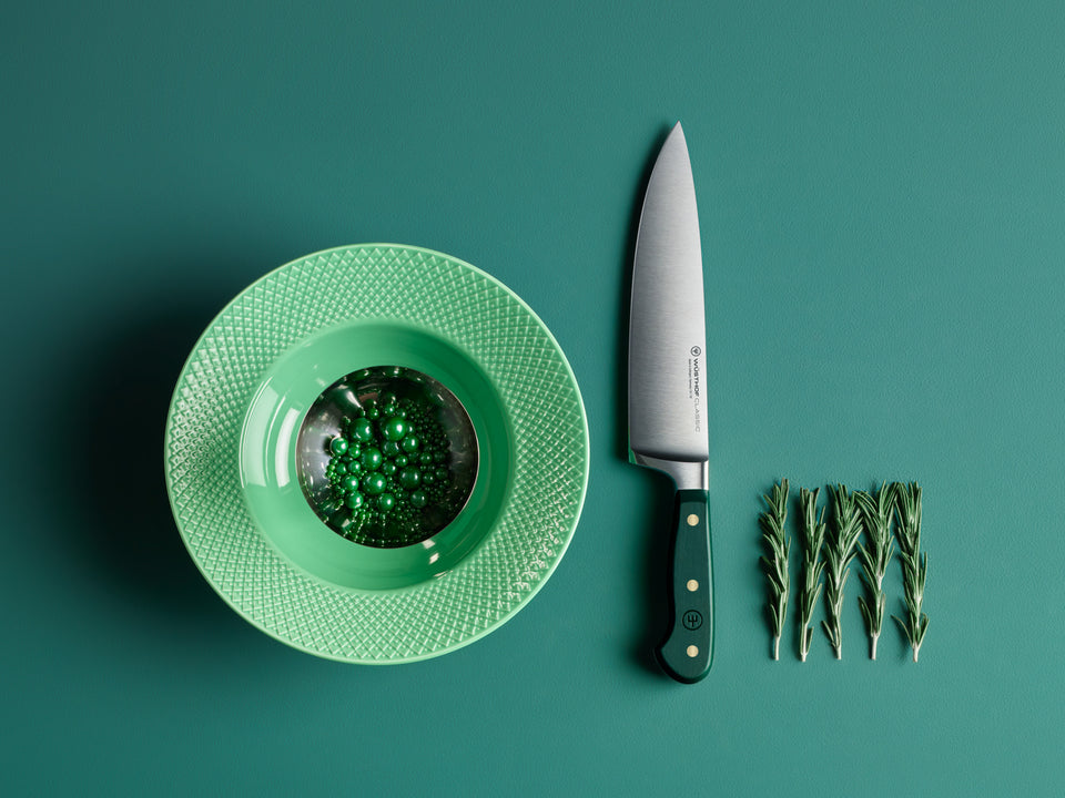 Green plate with a small dish, knife, and sprigs of greenery on a teal background