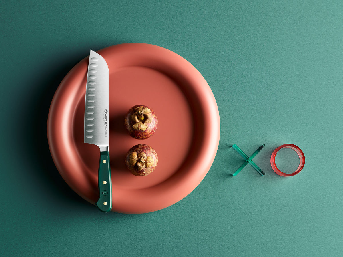 Knife on a red plate with two apples, next to green and red rings on a teal background