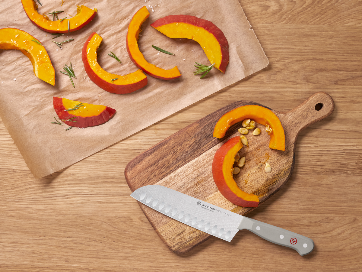 Sliced pumpkin on a wooden cutting board with a knife, on a wooden surface.