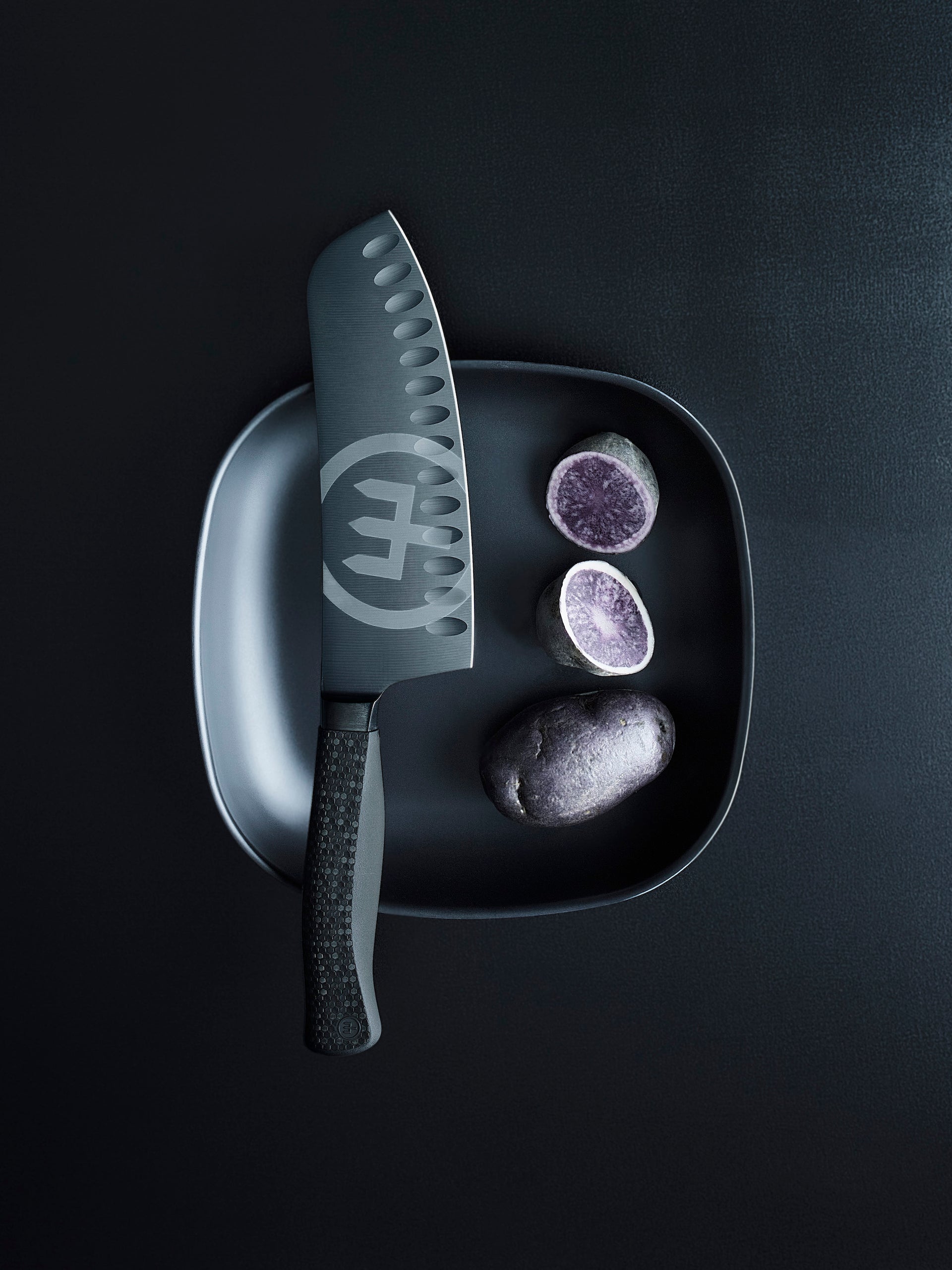 Gray knife with a brand logo on a black plate with gray and purple stones on a black background