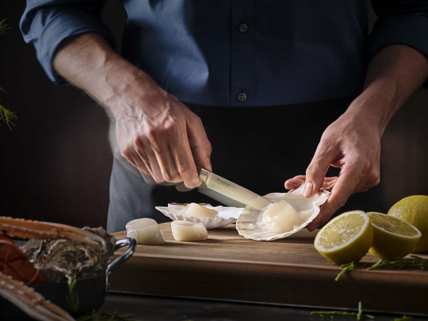 Person preparing scallops on a wooden cutting board with lemons and herbs.