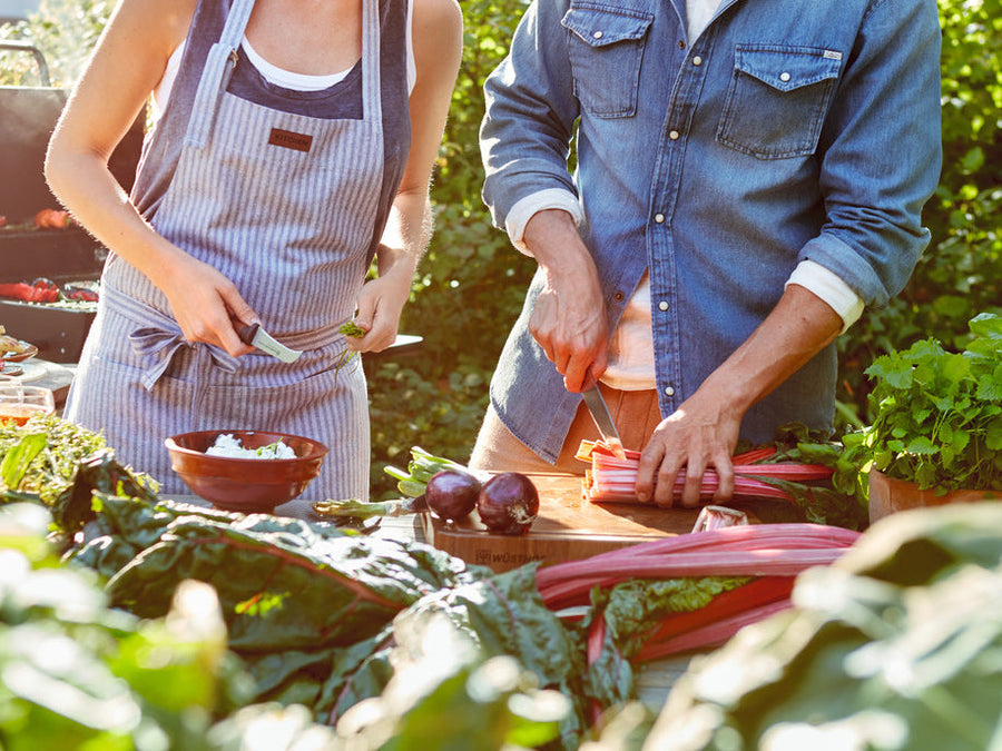 Two people preparing vegetables outdoors, surrounded by greenery.