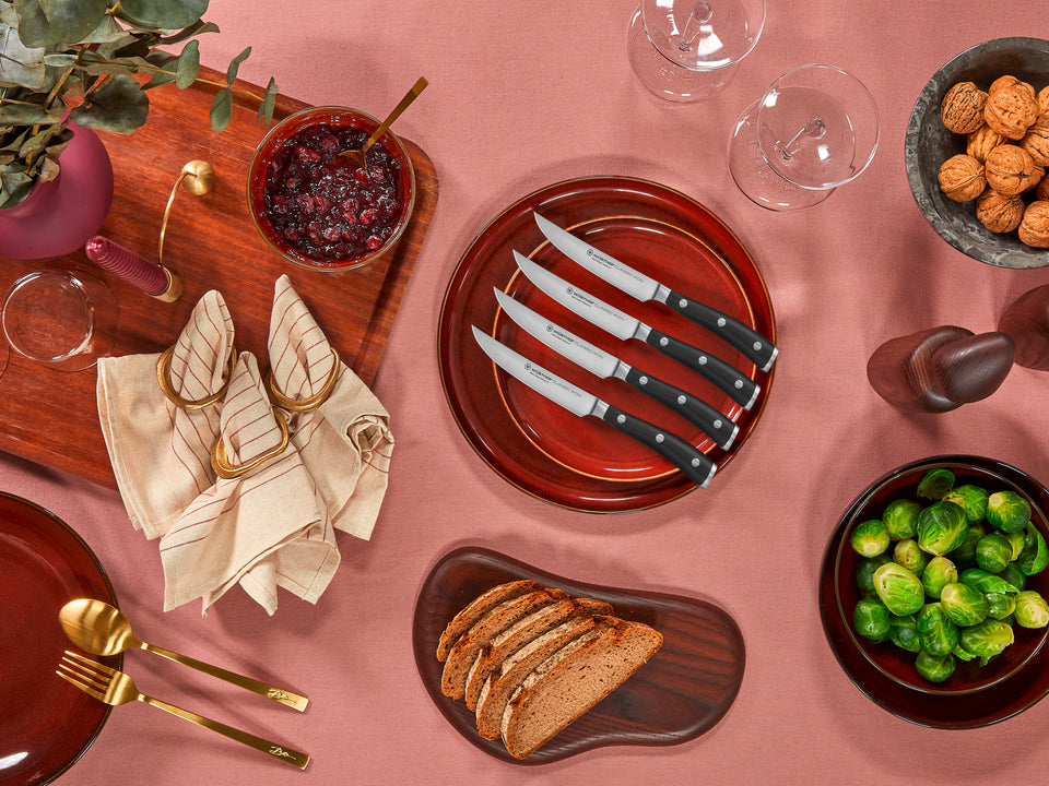 Table setting with bread, knives, and various dishes on a pink tablecloth.