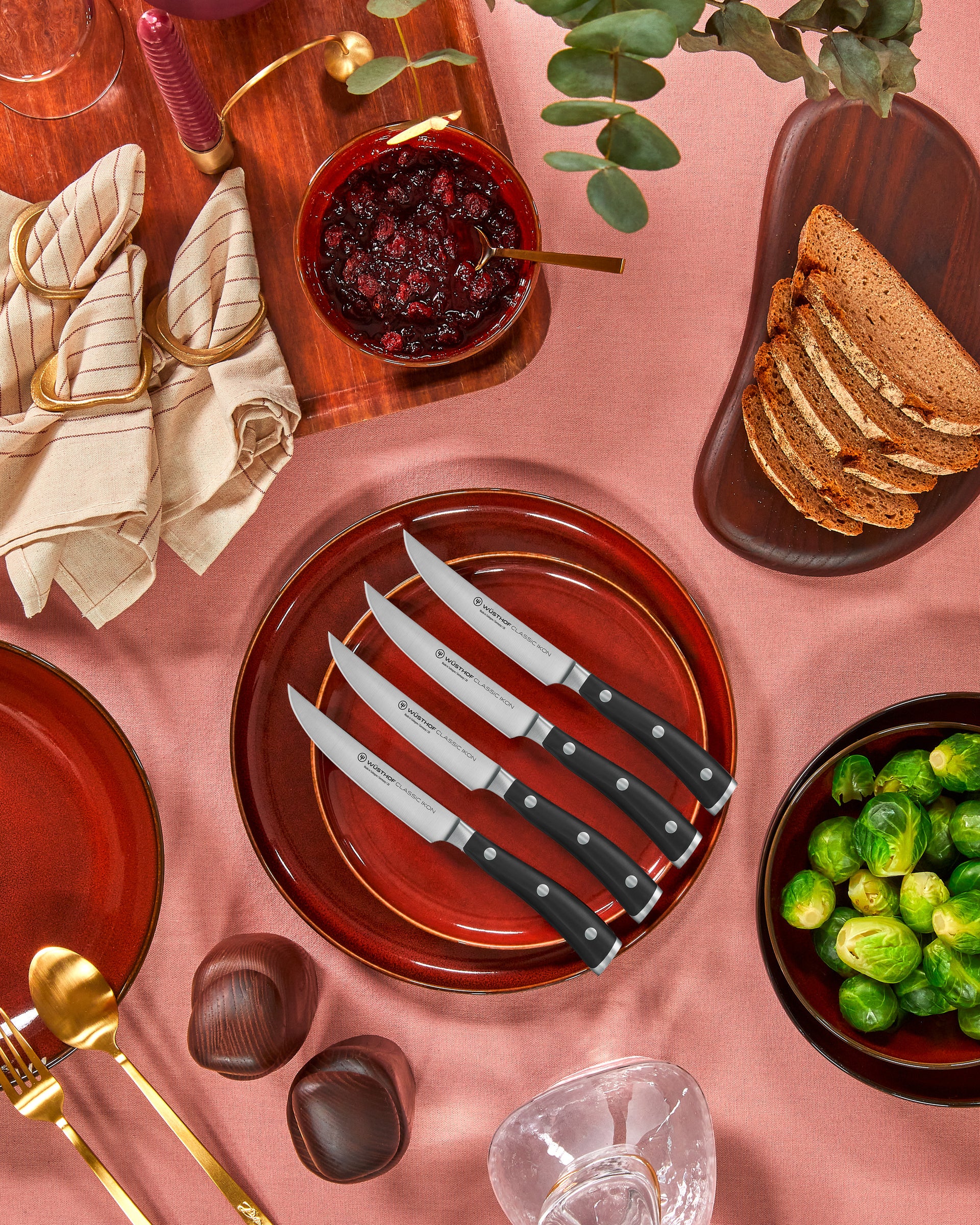 Table setting with red plates, knives, bread, and vegetables on a pink surface.