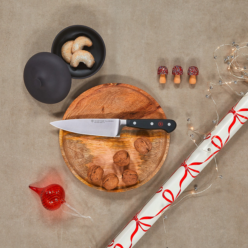 Wooden cutting board with knife, black container, and decorative items on a beige surface