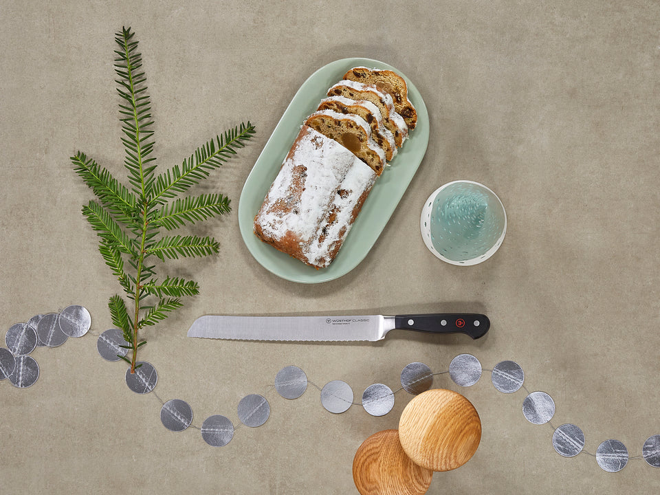 Loaf of bread with powdered sugar on a green plate, knife, and decorative elements on a beige background