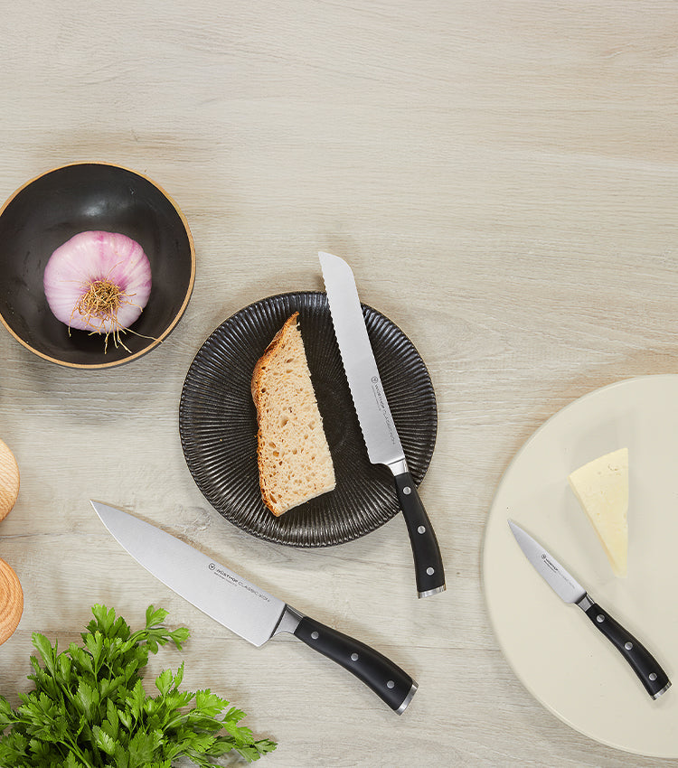 Knives on a table with bread, cheese, and herbs